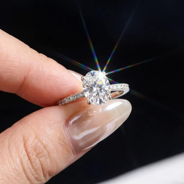 A close-up of a hand holding a silver-toned solitaire engagement ring with a sparkling round-cut diamond. The ring is shown against a dark background with a bright starburst effect around the gemstone.