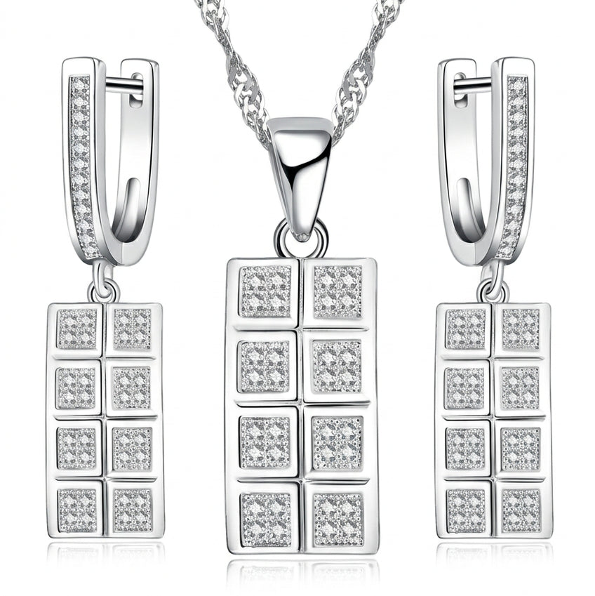 A silver-toned jewelry set featuring a rectangular pendant necklace, matching drop earrings, and a chain on a white background. The pendant and earrings are decorated with multiple small clear square stones.
