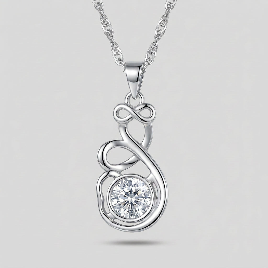 A silver-toned necklace with a pendant featuring an infinity symbol and a clear faceted gemstone, displayed on a dark textured surface with a folded navy blue fabric background.