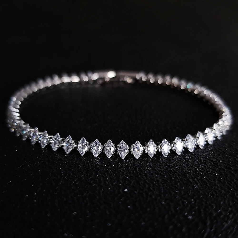 A silver tennis bracelet featuring marquise-cut clear gemstones, displayed on a textured black background.