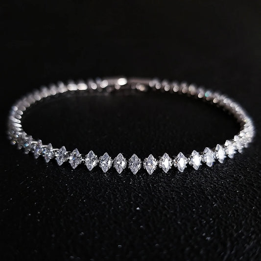 A silver tennis bracelet featuring marquise-cut clear gemstones, displayed on a textured black background.