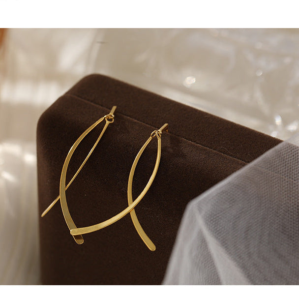 Gold earrings on a dark brown cushion with a soft, blurred background