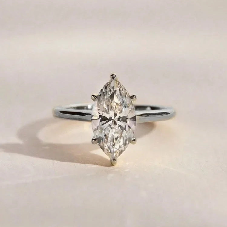 A silver-tone ring featuring a marquise-cut clear gemstone in a prong setting, photographed on a clean, light beige background.