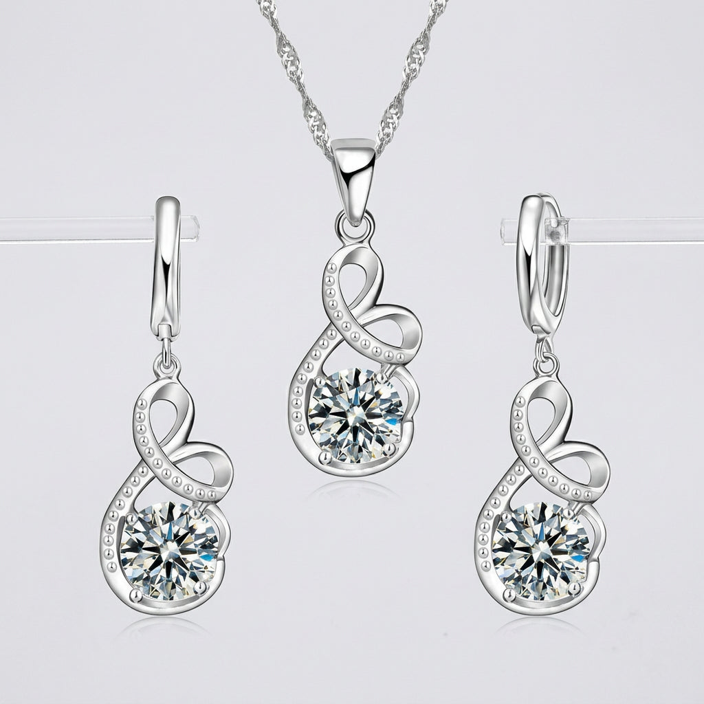 Silver necklace and matching drop earrings set with heart-shaped bezel settings and round clear gemstones, shown on a white background with repeated store watermark text.