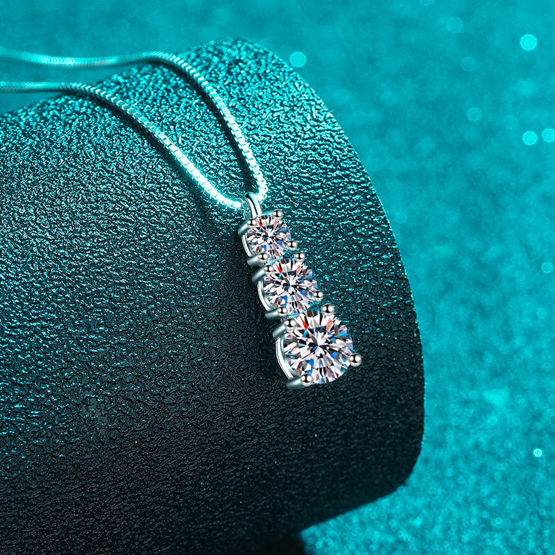 Silver necklace with a three-heart-shaped gemstone pendant on a textured green surface.